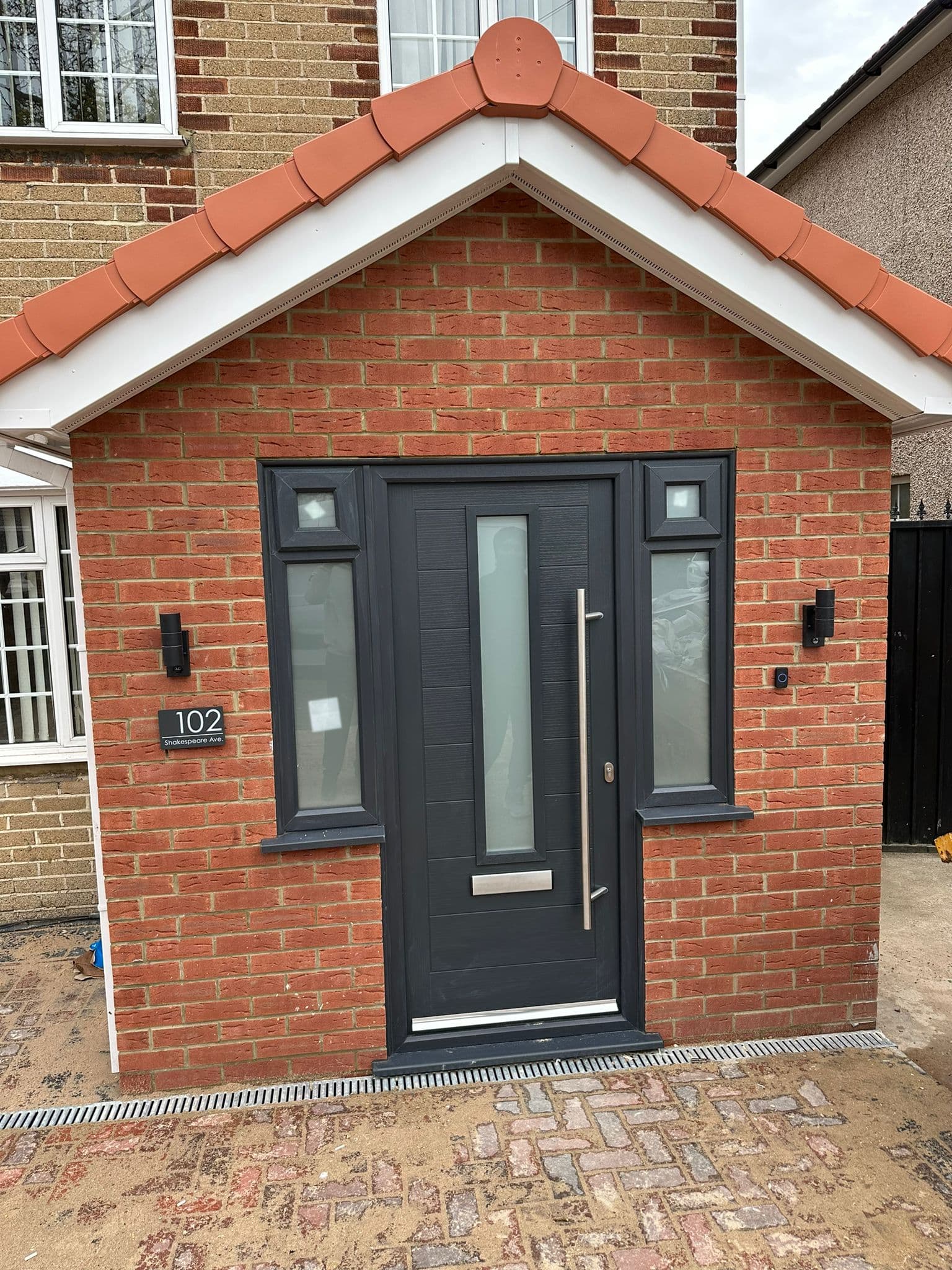 Anthracite composite front door with contemporary design and chrome hardware in a modern porch