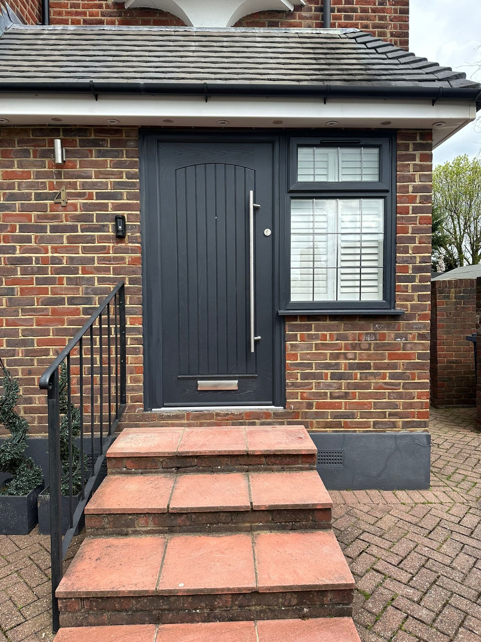 Anthracite composite entrance door with iron railing and brick steps