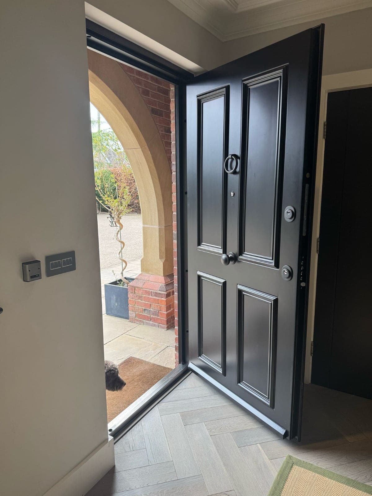 Black steel door open showing herringbone parquet interior