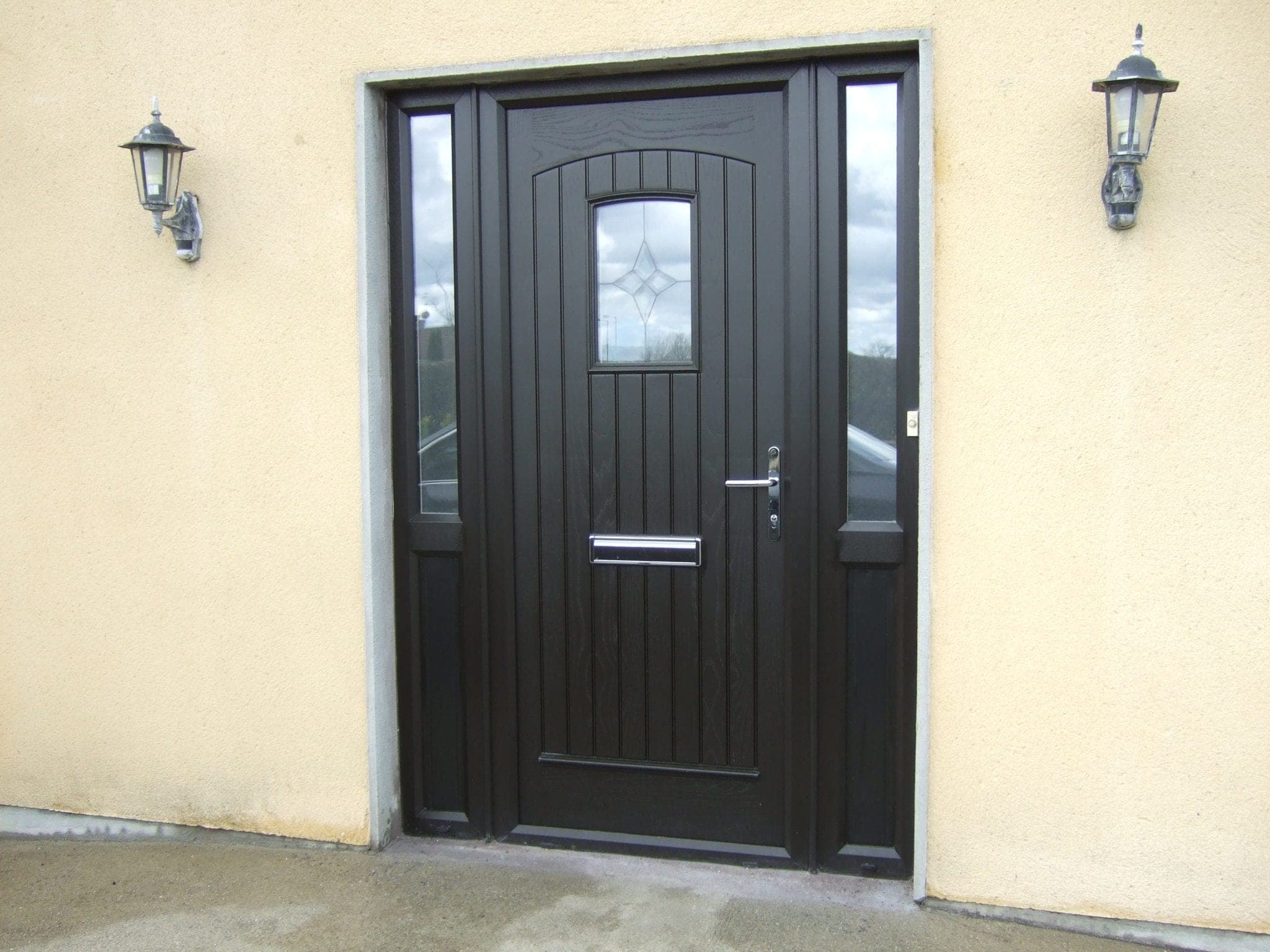 Palladio black composite entrance door with twin patterned-glass sidelights and coach lanterns on a render-clad porch