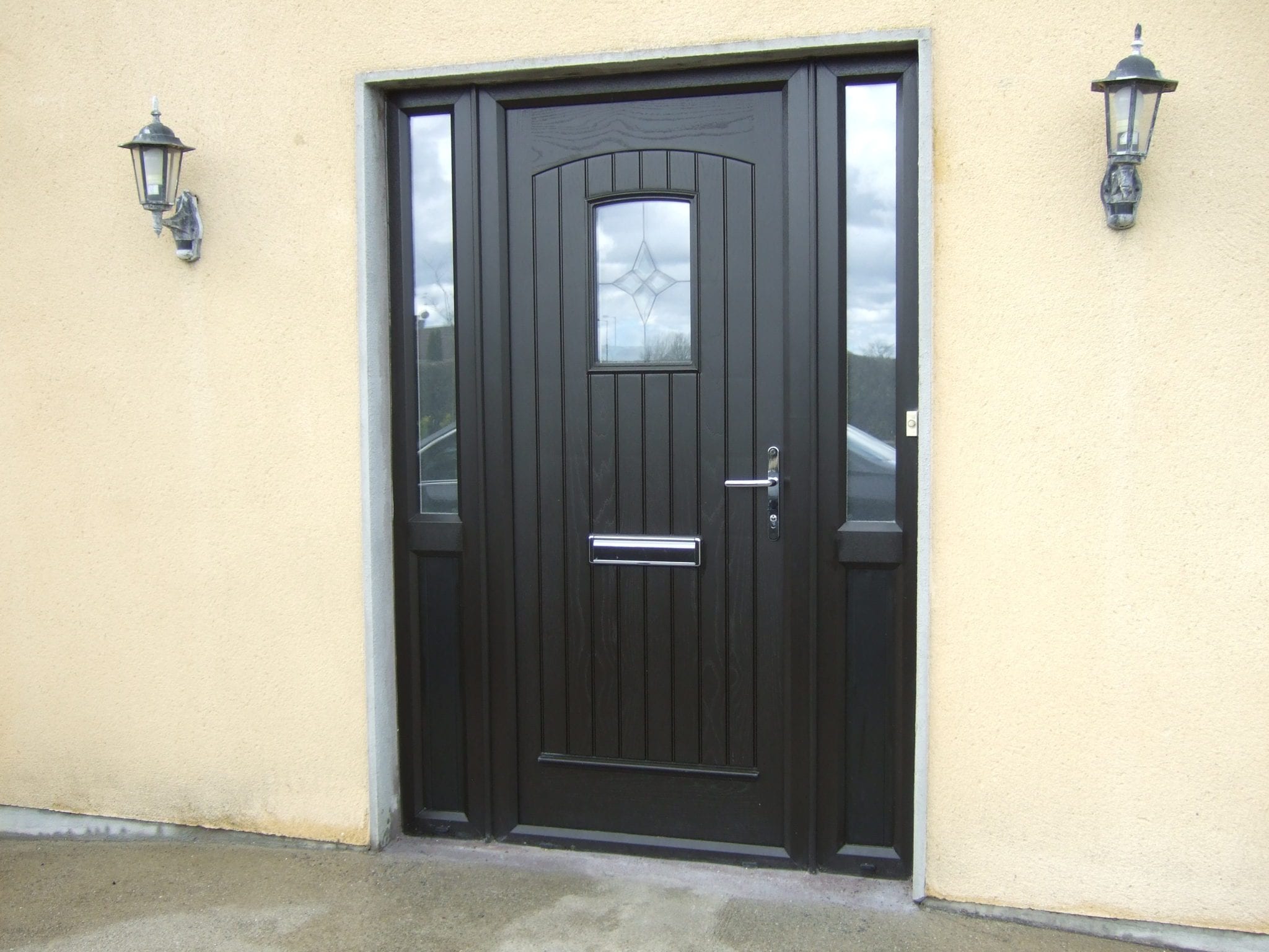 Palladio black composite entrance door with twin patterned-glass sidelights and coach lanterns on a render-clad porch